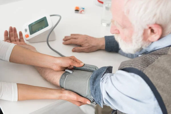 Ausgeschnittene Ansicht einer Krankenschwester, die den Blutdruck eines älteren Mannes misst — Stockfoto