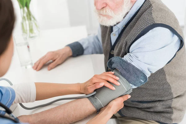 Ausgeschnittene Ansicht einer Krankenschwester, die einem grauhaarigen Mann die Hände aufsetzt und den Blutdruck misst — Stockfoto