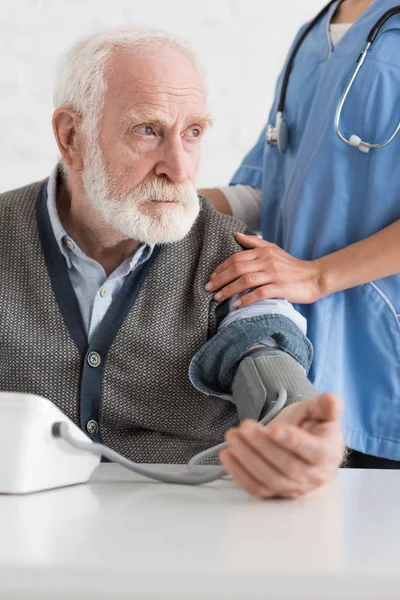 Vue recadrée de l'infirmière mettant la main sur l'homme aux cheveux gris, mesurant la pression artérielle — Photo de stock