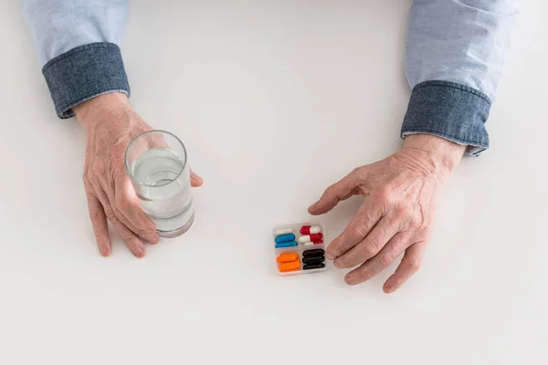 Vue recadrée d'un homme âgé tenant du verre avec de l'eau et des pilules dans les mains — Photo de stock