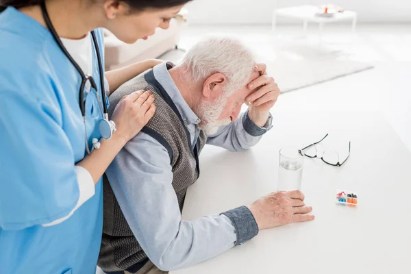 Vista de alto ángulo de la enfermera poniendo las manos en el hombre de pelo triste y gris - foto de stock