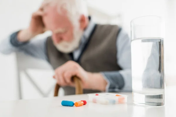Selective focus of pills and water in glass on sad senior man background — Stock Photo
