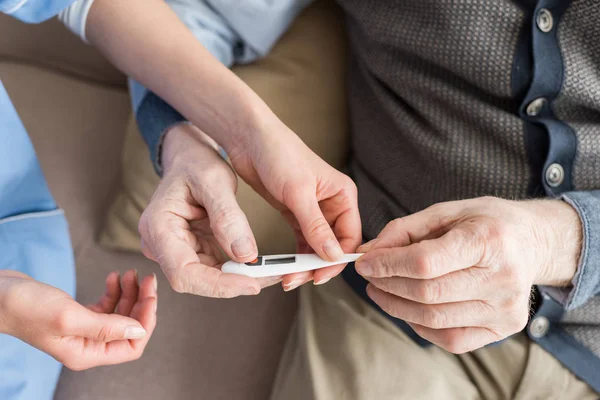 Cropped view of elderly man holding thermometer in hands — Stock Photo