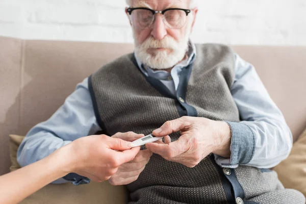 Vista recortada de la mano de la mujer que da termómetro al hombre de edad avanzada - foto de stock