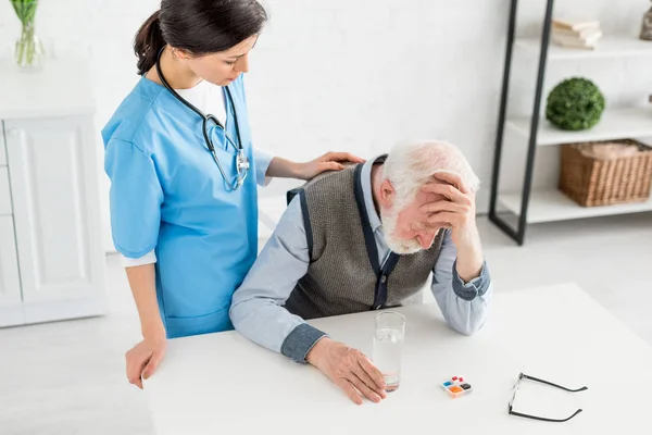 High angle view of nurse putting hands on sad grey haired man — Stock Photo