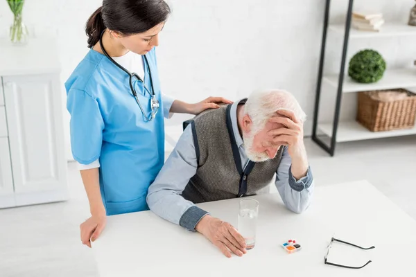 Vista ad alto angolo di infermiera mettendo le mani su triste uomo dai capelli grigi — Foto stock