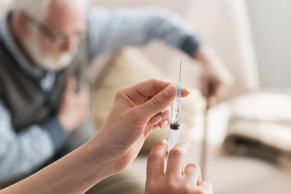 Selective focus of woman hands with syringe on elderly man background — Stock Photo