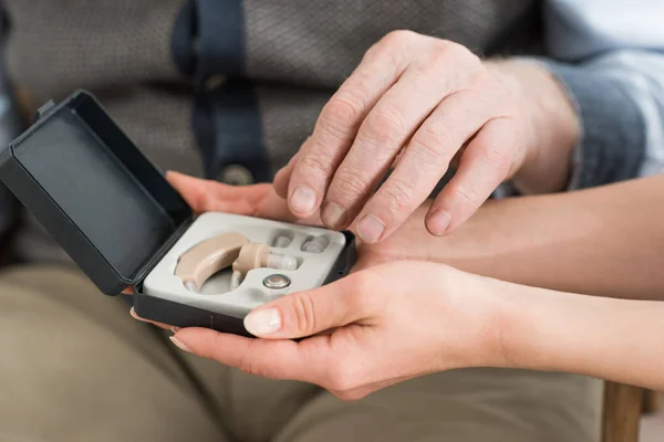 Close up view of hearing aid box in woman and senior man hands — Stock Photo