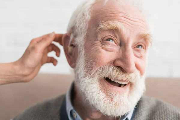 Mano donna che aiuta l'uomo dai capelli grigi, indossando apparecchi acustici — Foto stock