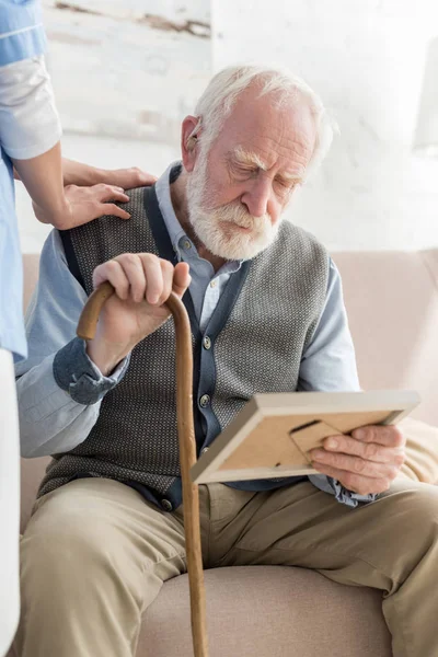 Nurse standing near upset grey haired man with photo frame, putting hands on his shoulder — Stock Photo
