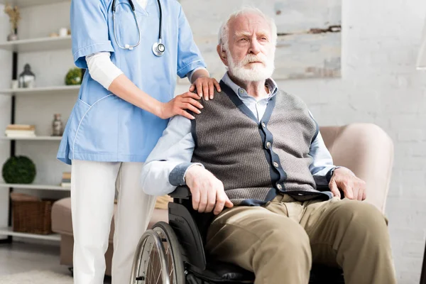 Doctor putting hands on disabled senior man in wheelchair — Stock Photo