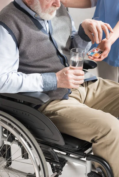 Vista cortada do médico dando pílulas para o homem idoso com deficiência em cadeira de rodas — Fotografia de Stock