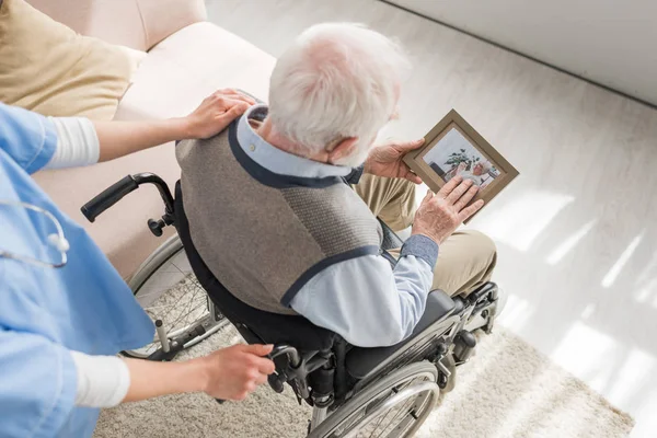 Vue en angle élevé de l'infirmière debout derrière un homme aux cheveux gris handicapé en fauteuil roulant — Photo de stock