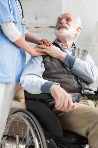 Arzt hält Hand an fröhlichen und behinderten Senioren im Rollstuhl — Stockfoto