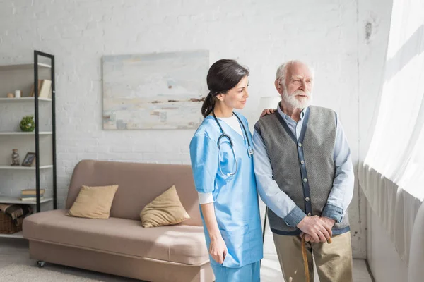 Arzt schaut weg, steht mit älterem Mann im Haus mit Kopierraum — Stockfoto