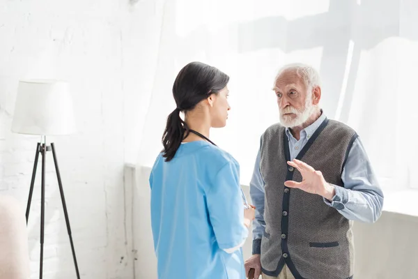 Senior man standing inside home with copy space, and talking with nurse — Stock Photo