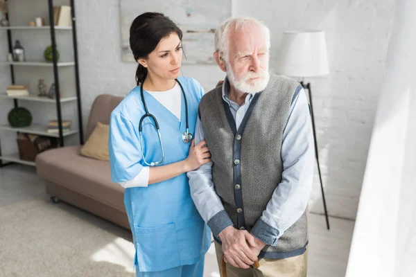 Medico di sostegno di uomo anziano, in piedi in una stanza luminosa, guardando da parte — Foto stock