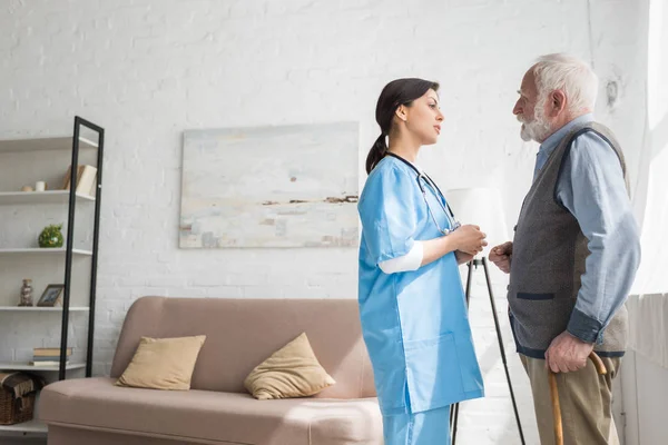 Grey haired man talking to nurse, standing in room with copy space — Stock Photo