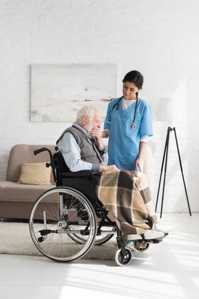 Nurse standing near tired and disabled senior man in wheelchair — Stock Photo