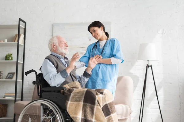 Nurse talking to disabled and happy grey haired man in wheelchair — Stock Photo