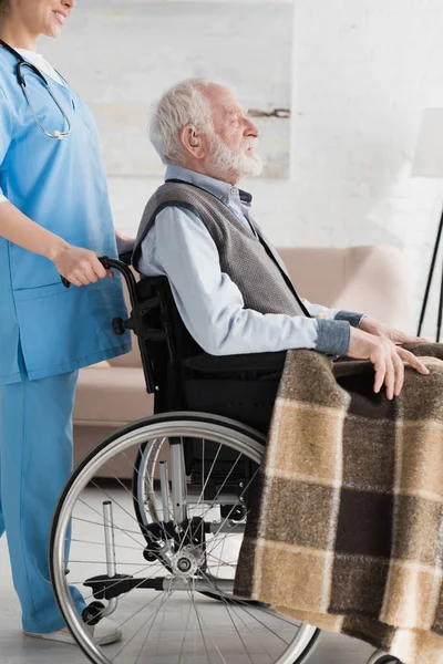 Cropped view of nurse carrying about disabled and grey haired man in wheelchair — Stock Photo