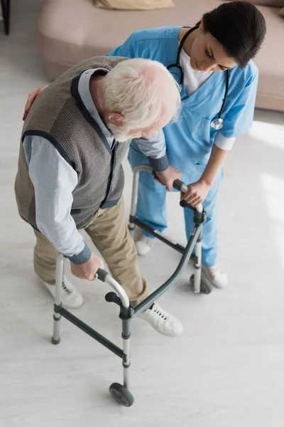 Высокий угол обзора врача, помогающего старику ходить, выздоравливая после травмы — стоковое фото