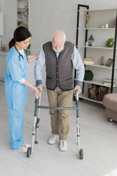 Médico ayudando a un hombre retirado a caminar, y recuperándose después de una lesión - foto de stock