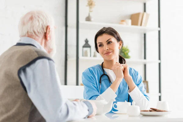 Happy doctor sitting on kitchen with senior man — Stock Photo