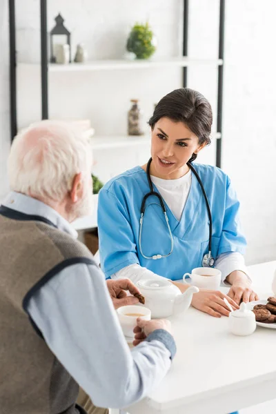 Hochwinkelaufnahme einer Krankenschwester, die mit einem grauhaarigen Mann spricht, der in der Küche sitzt — Stockfoto