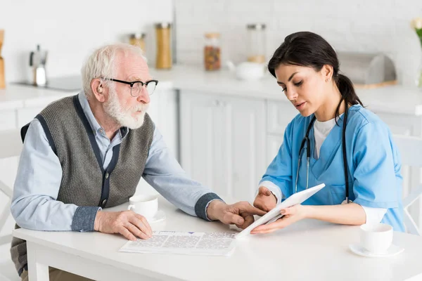 Grauhaariger Mann spricht mit Krankenschwester in Küche und nutzt digitales Tablet — Stockfoto