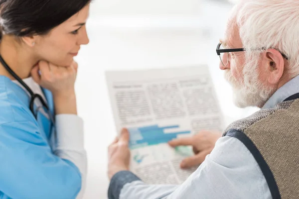 Focus selettivo dell'uomo dai capelli grigi che parla con l'infermiera, tenendo il giornale in mano — Foto stock