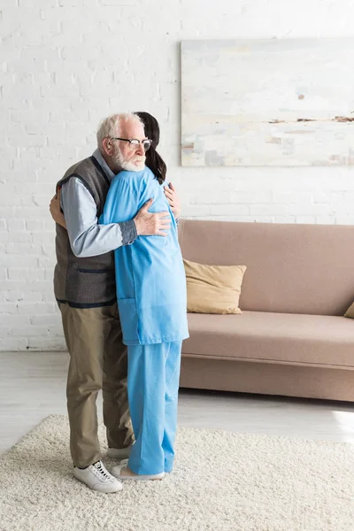 Calm senior man hugging with nurse, standing in bright room — Stock Photo