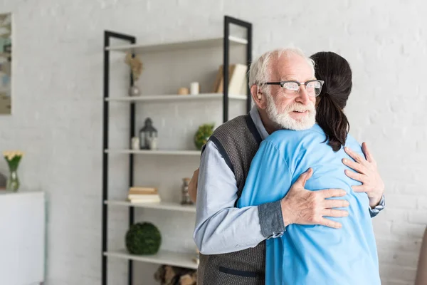 Щасливий пенсіонер обіймається з лікарем, стоячи в світлій кімнаті — стокове фото