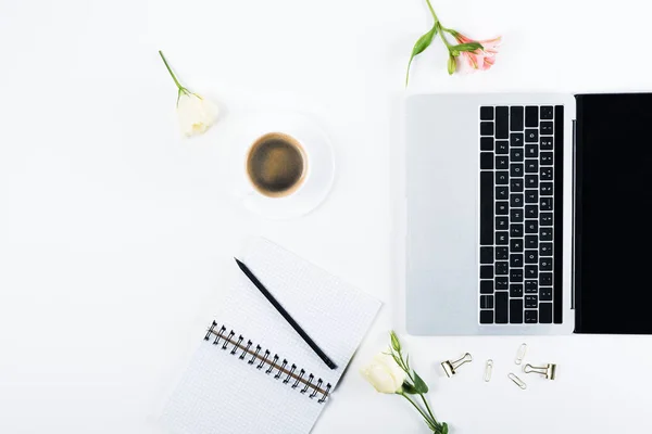 Top view of laptop with blank screen, notebook with pen, paper clips, binder clips, flowers and cup of coffee on white — Stock Photo