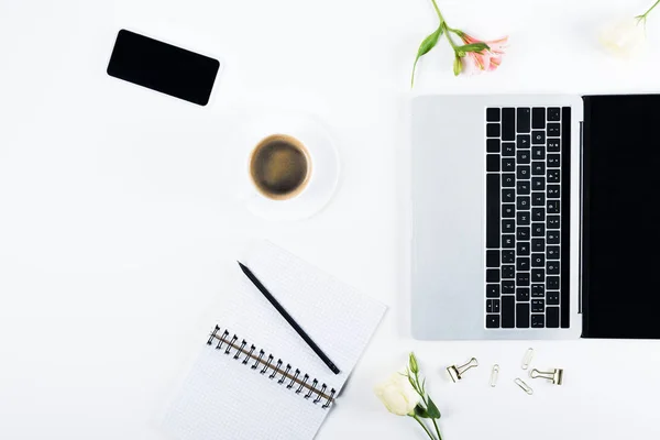 Ansicht von Laptop und Smartphone mit leerem Bildschirm, Notizbuch mit Stift, Büroklammern, Ordnerklammern, Blumen und Kaffeetasse auf weiß — Stockfoto