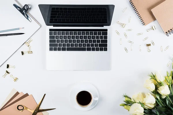 Top view of laptop with blank screen, cup of coffee, clipboard, flowers, pen, pencil, scissors, binder clips and paper clips of white — Stock Photo