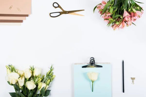 Top view of clipboard, flowers, scissors, pen, paper clips, binder clip and craft paper on white — Stock Photo