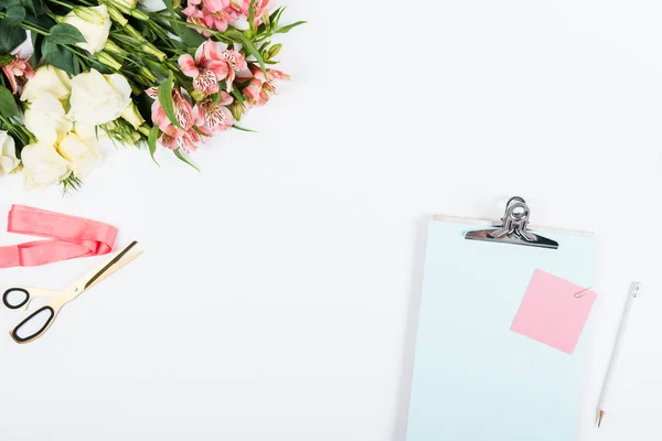 Vue de dessus des fleurs, presse-papiers, ciseaux, ruban, papier et crayon sur blanc — Photo de stock