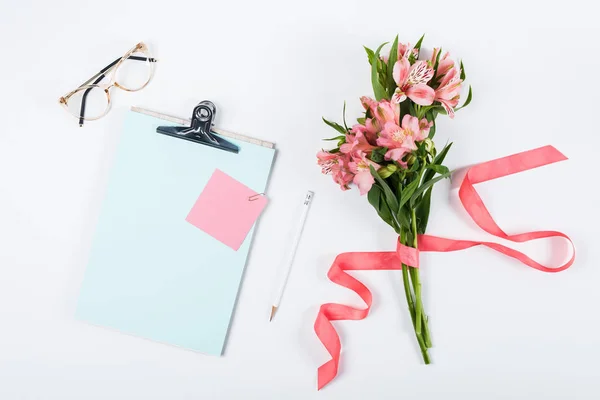 Vista superior de flores, portapapeles, gafas, cinta, papel y lápiz en blanco - foto de stock