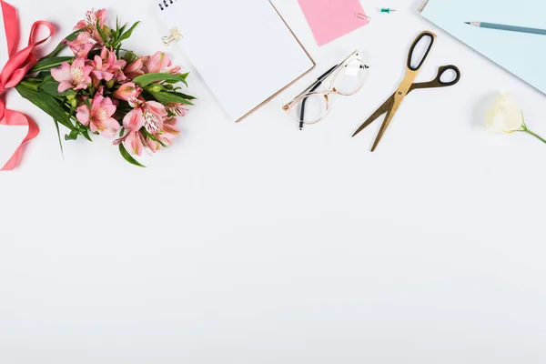 Vista dall'alto di fiori con nastro, appunti, forbici, quaderno, matita e bicchieri su bianco — Foto stock