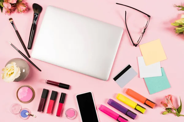 Vue du haut de l'ordinateur portable, smartphone avec écran vierge, carte de crédit, lunettes, fleurs et cosmétiques décoratifs sur rose — Photo de stock