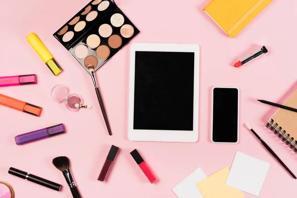 Вид сверху на цифровой планшет и смартфон с чистым экраном, ноутбуки и декоративная косметика на розовом — стоковое фото