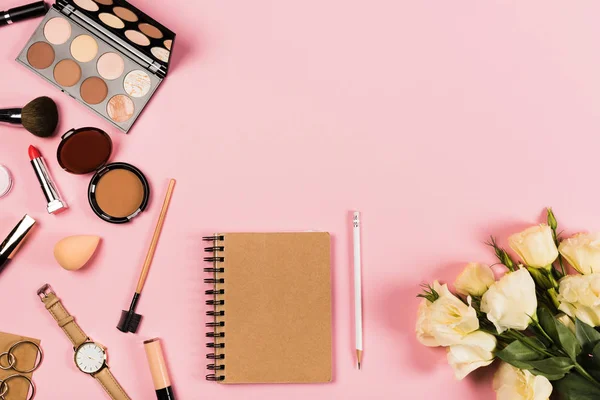 Верхний вид наручных часов, серьги, цветы, ноутбук, карандаш и декоративная косметика на розовый — стоковое фото