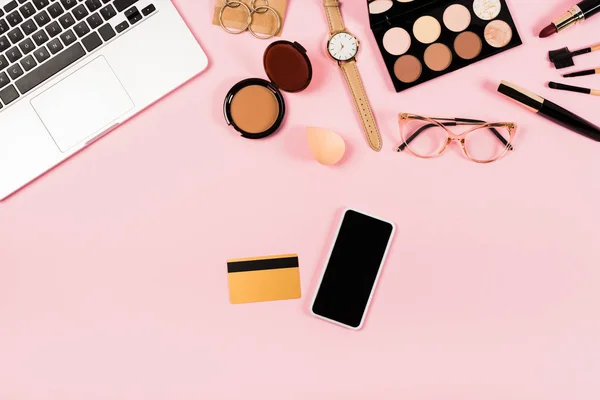 Vista superior do laptop, smartphone com tela em branco, cartão de crédito e cosméticos decorativos em rosa — Fotografia de Stock