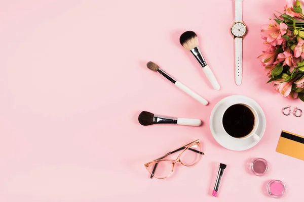 Cama plana con taza de café, flores, cosméticos decorativos, tarjeta de crédito y accesorios en rosa - foto de stock