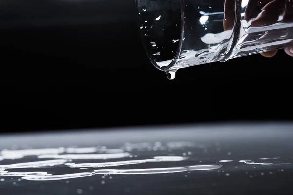 Vista recortada de la mujer sosteniendo manchas de vidrio y agua en la superficie oscura - foto de stock