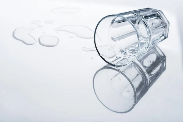 Glass with spilled water and drops on light surface — Stock Photo