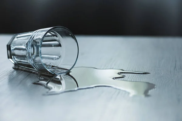 Glass with spilled water on textured wooden surface — Stock Photo