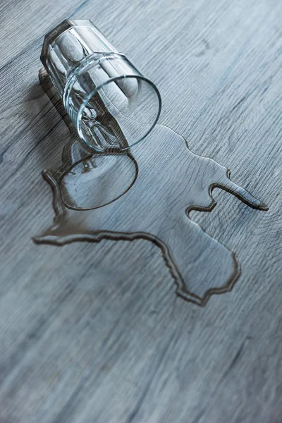 Verre avec de l'eau renversée sur une surface en bois texturé — Photo de stock