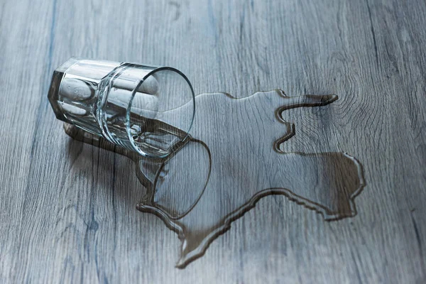 Glass with spilled water on textured wooden surface — Stock Photo